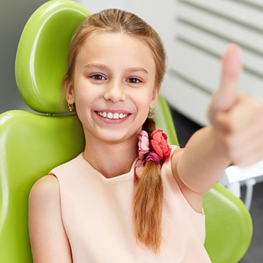 Little girl in dental chair giving thumbs up