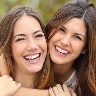 Two female teenagers smiling and hugging after seeing a dentist for teens in Midland