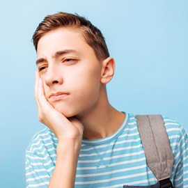 A teenage boy wearing a backpack and holding his cheek in pain