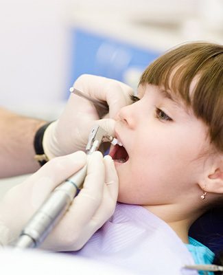 A young girl sits in a dental chair while a dentist cleans her teeth, surrounded by dental tools and equipment.