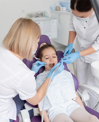 A young girl sits in a dental chair while a dentist examines her teeth during a routine check-up.