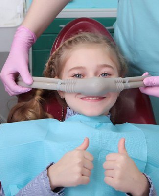 A little girl in a dentist chair smiles and gives a thumbs up, showing confidence during her dental visit.