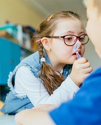 A young girl with glasses brushes her teeth, promoting good dental hygiene practices.
