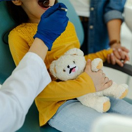 child holding teddy bear while visiting dentist 
