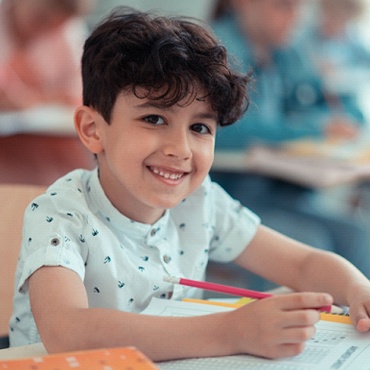 A young boy sits at a desk and smiles after seeing a dentist for kids in Midland