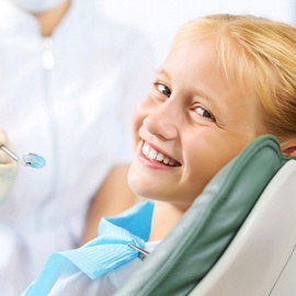 A girl with blonde hair smiles as the dentist prepares to look at her teeth and apply fluoride