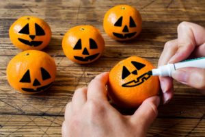 hand drawing jack-o-lantern faces on oranges