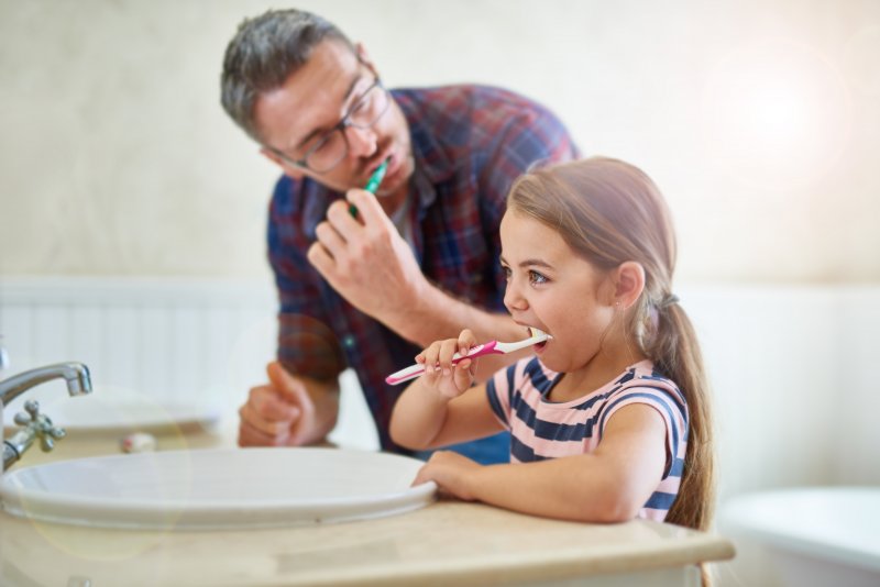 A father and daughter brushing together to fight teeth sensitivity