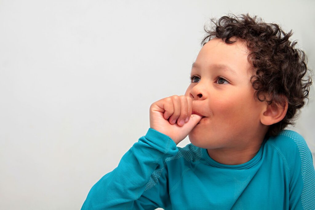 Little boy with curly hair in teal shirt sucking his thumb